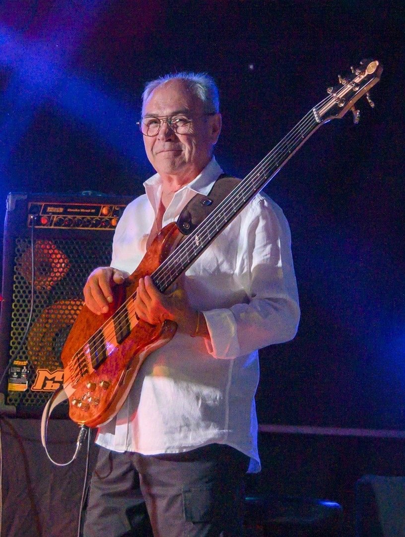 Le bassiste d'Arkanciel en chemise blanche, sa basse cinq cordes en main, devant son ampli.