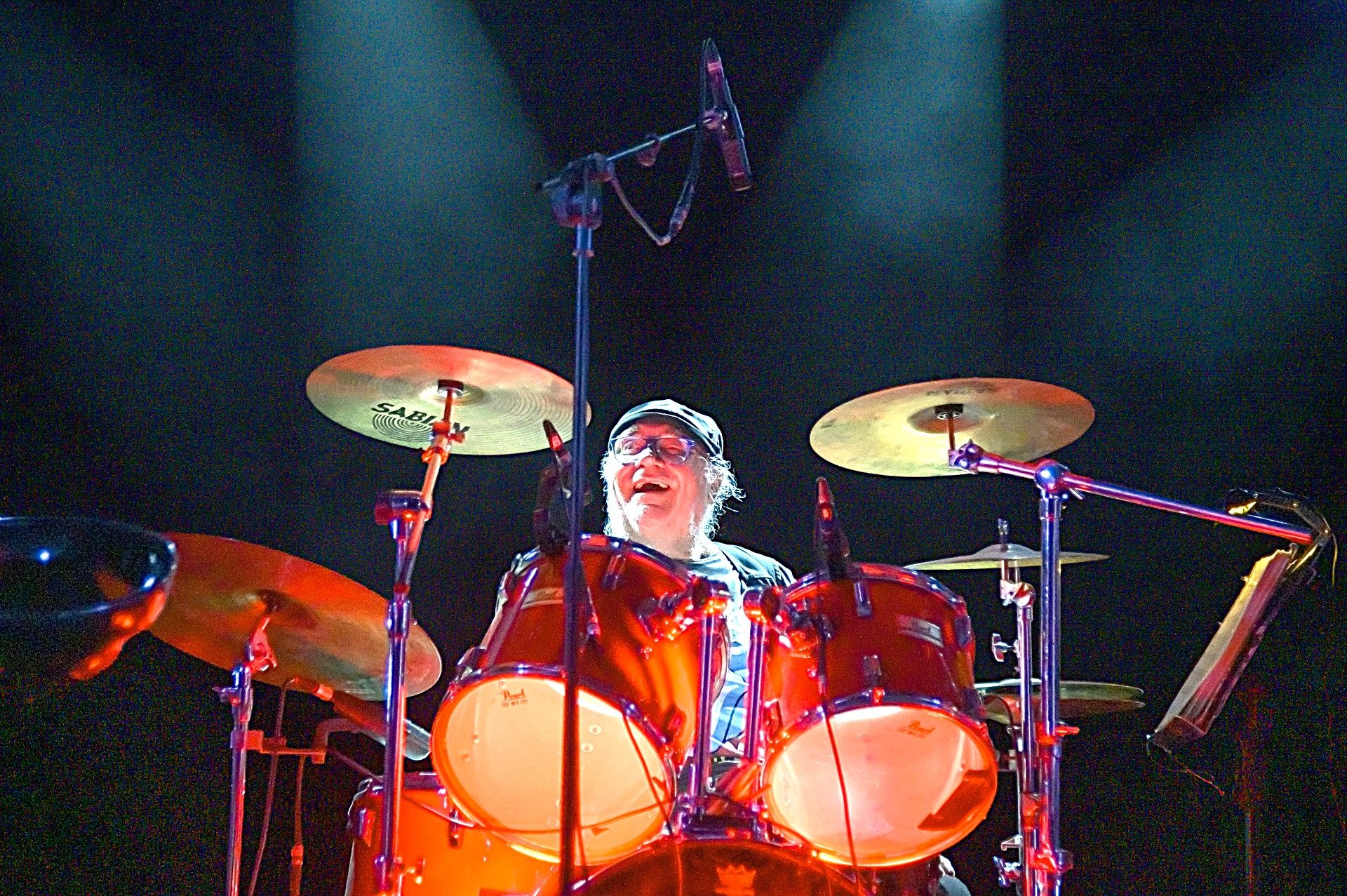 Le batteur d'Arkanciel entre ses cymbales, casquette sur la tête, éclairé en rouge.