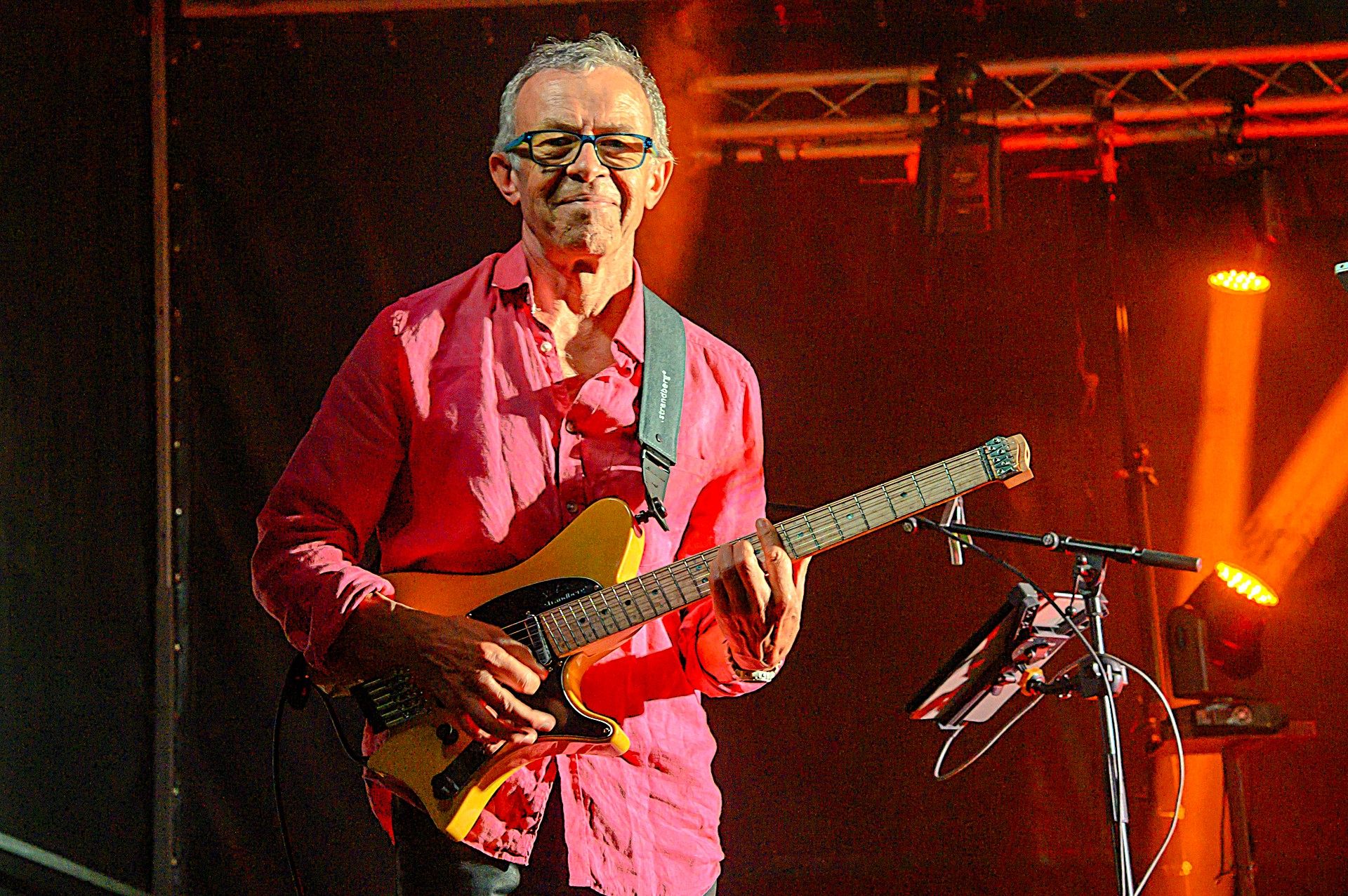 Le guitariste d'Arkanciel en chemise rose, guitare dorée en main, sous une lumière orangée.